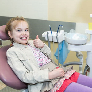 Young girl in dental treatment chair, making thumbs-up gesture