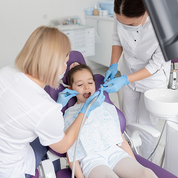 Dentist and assistant applying dental sealants to child’s teeth