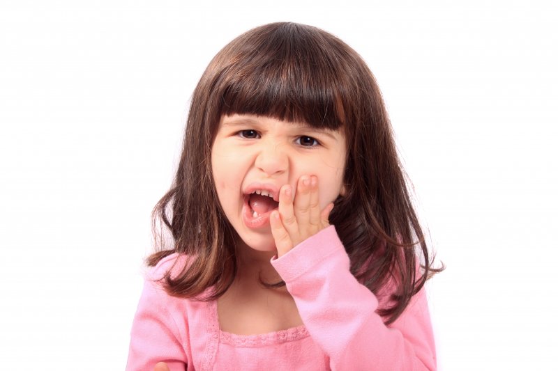 Child holding their cheek needing a tooth extraction