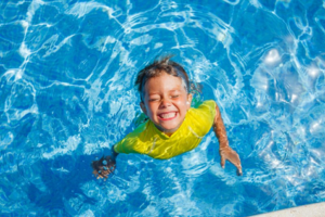 Downward shot of a young boy standing in pool, grinning wide